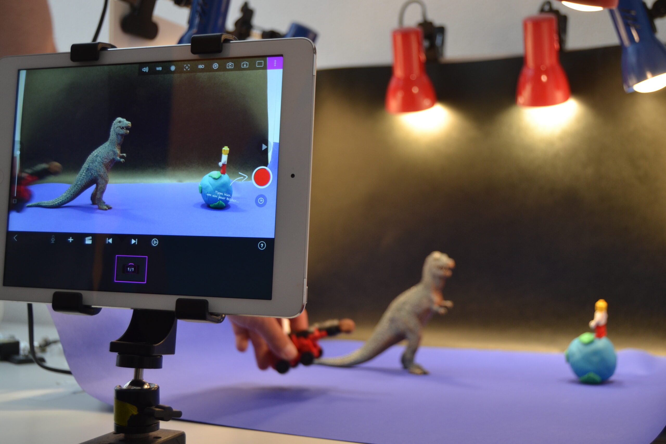 Im Vordergrund: iPad mit Trickfilm-App. Im Hintergrund: Trickfilmbühne mut Dinosaurier und Legomännchen